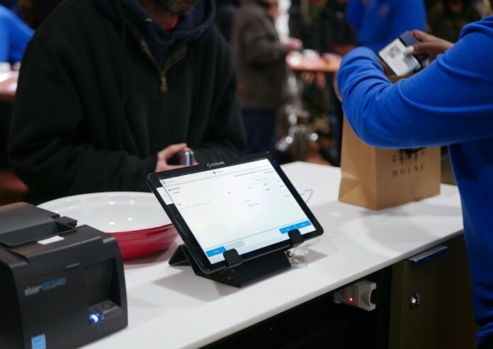 A budtender checks out a cannabis customer at a dispensary sales counter. A lit tablet displaying Cova's point of sale software sits between them to use for transactions.