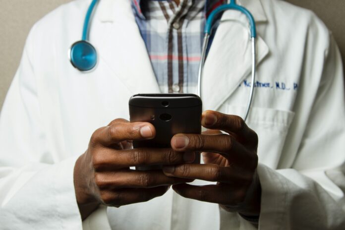 Doctor Holding Cell Phone. Cell phones and other kinds of mobile devices and communications technologies are of increasing importance in the delivery of health care. Photographer Daniel Sone